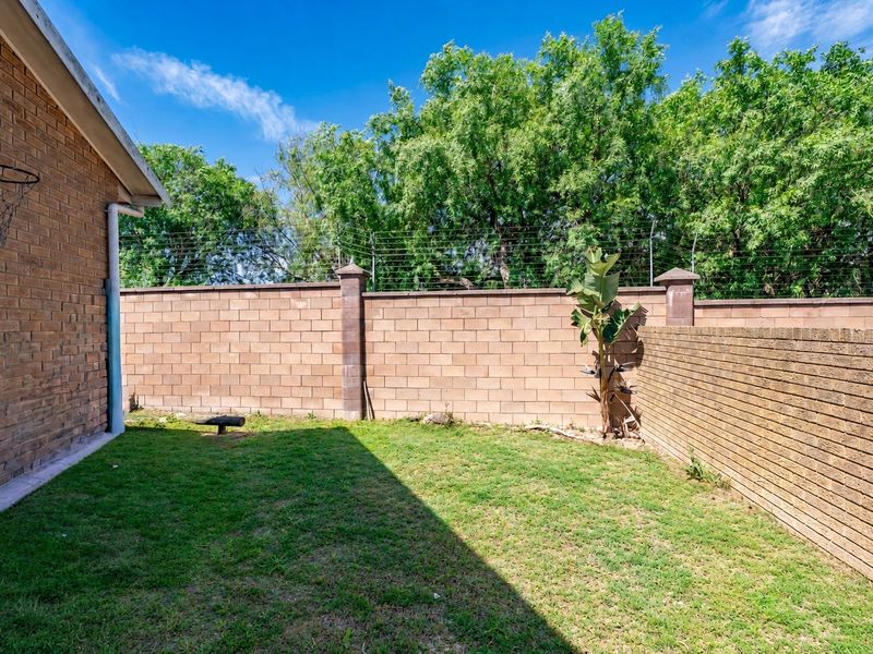 A private rear garden featuring a well-maintained lawn, enclosed by high brick boundary walls with integrated electric security fencing.
