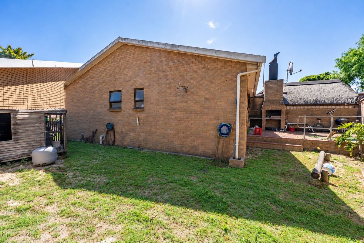 Rear exterior view of the property featuring a brick facade, a built-in braai area, and a small garden space.