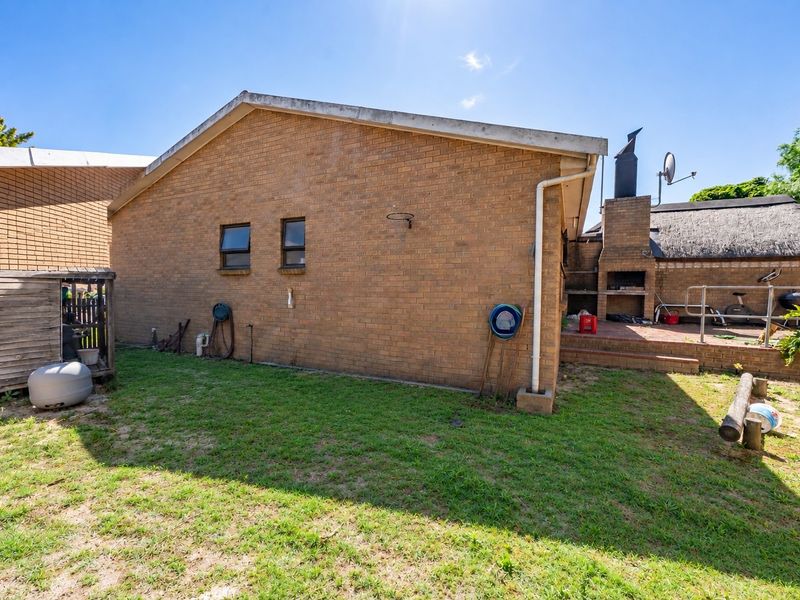 Rear exterior view of the property featuring a brick facade, a built-in braai area, and a small garden space.