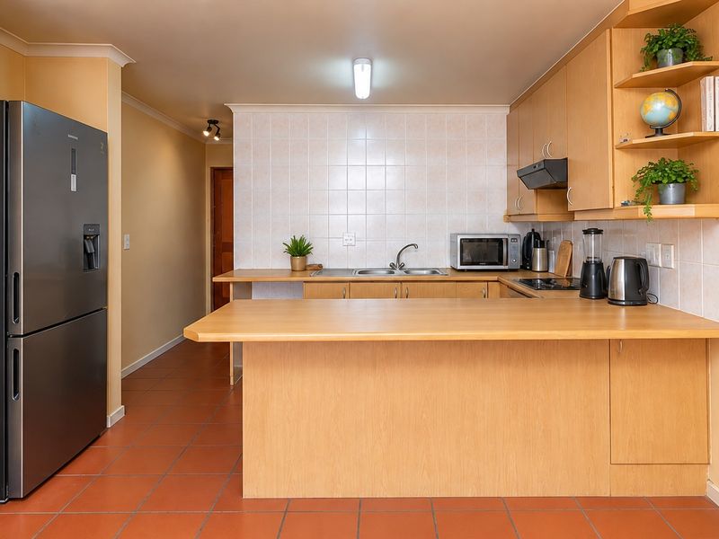 Functional kitchen featuring light wood cabinetry, a breakfast bar, tiled backsplash, and terracotta flooring, offering a practical layout for daily meal preparation.