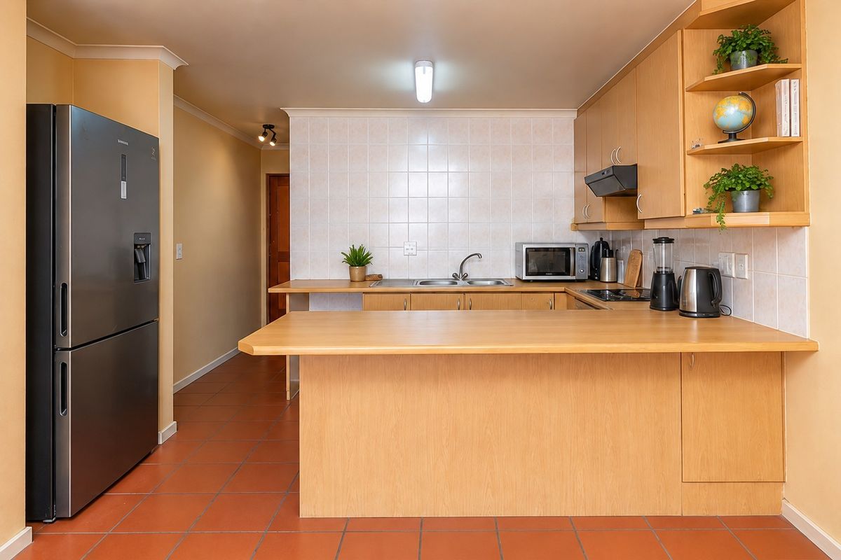 Functional kitchen featuring light wood cabinetry, a breakfast bar, tiled backsplash, and terracotta flooring, offering a practical layout for daily meal preparation.