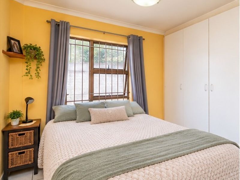 A bedroom featuring built-in cupboards, tiled flooring, and security bars on the window, finished with bright yellow wall paint.