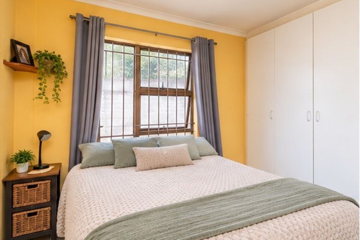 A bedroom featuring built-in cupboards, tiled flooring, and security bars on the window, finished with bright yellow wall paint.