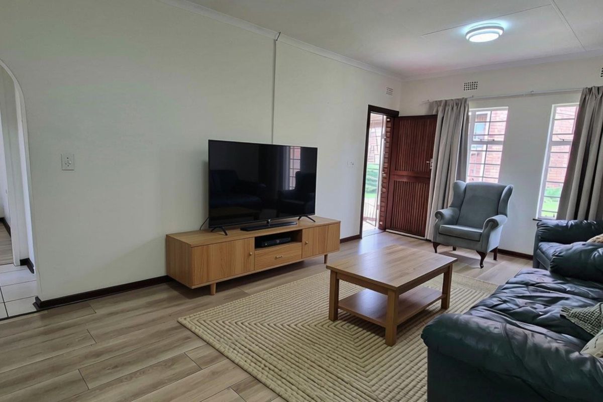 A bright and functional living room featuring laminate flooring, an arched entryway, and natural light through the windows.