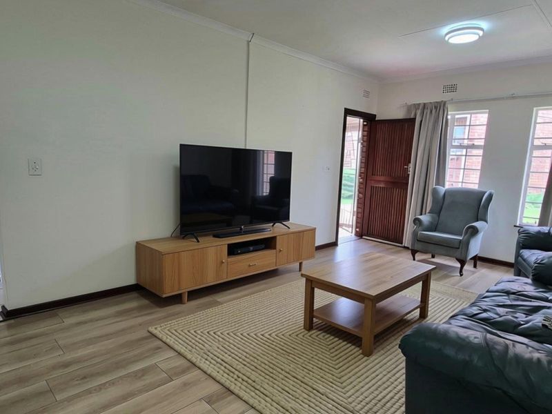 A bright and functional living room featuring laminate flooring, an arched entryway, and natural light through the windows.