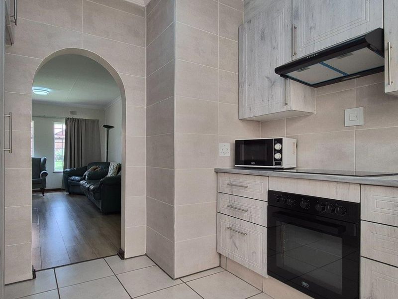 A functional kitchen featuring light wood-grain cabinetry, built-in oven, extractor fan, and tiled finishes, leading through an arched doorway into the living area.