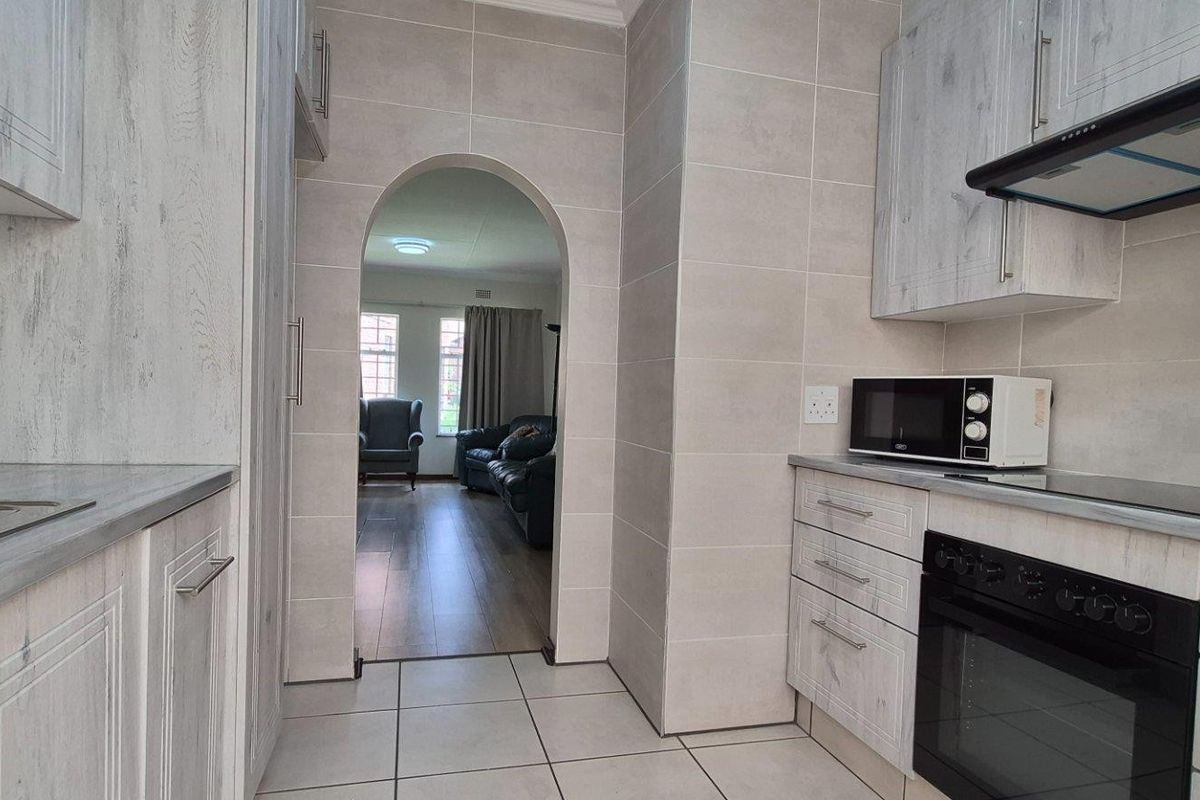 Modern kitchen featuring light wood-grain cabinetry, built-in oven, extractor fan, and tiled finishes, with an arched doorway leading to the adjacent living area.
