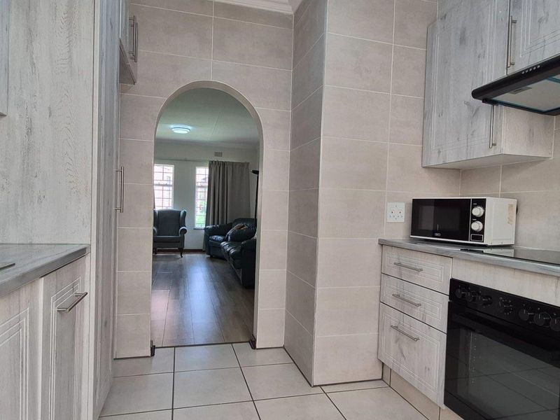 Modern kitchen featuring light wood-grain cabinetry, built-in oven, extractor fan, and tiled finishes, with an arched doorway leading to the adjacent living area.