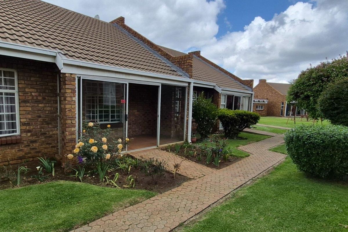 A well-maintained face brick exterior featuring a tiled roof, sliding glass doors, and a paved walkway leading through a landscaped garden area.