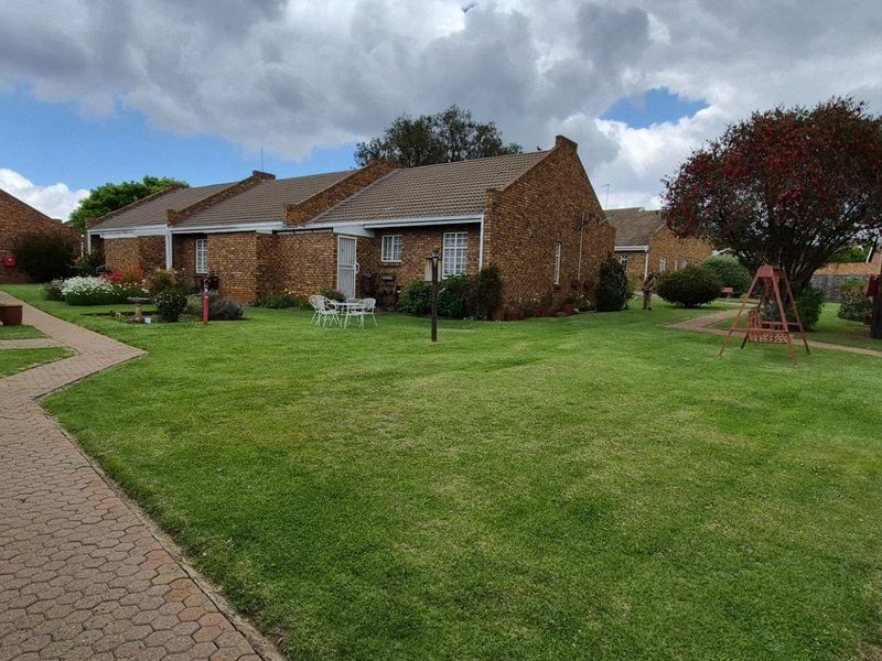 A well-maintained residential complex featuring face brick exteriors, tiled roofs, and paved walkways set within a spacious, landscaped communal garden area.