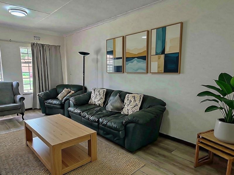 A well-maintained living room featuring laminate flooring, coved ceilings, and large windows that provide ample natural light.