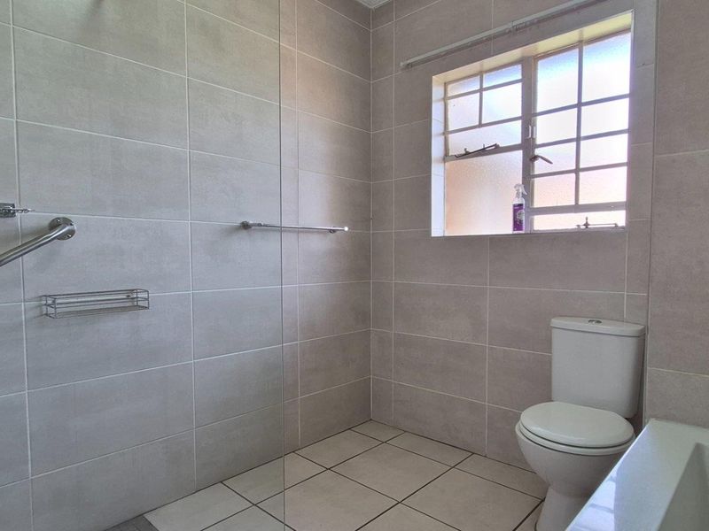 A clean, modern bathroom featuring a walk-in shower with a glass screen, neutral wall and floor tiling, and a standard toilet.