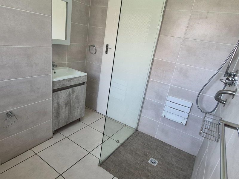 Modern bathroom featuring neutral wall tiles, a vanity cabinet with basin, a glass-enclosed shower with a wall-mounted seat, and contemporary fixtures.