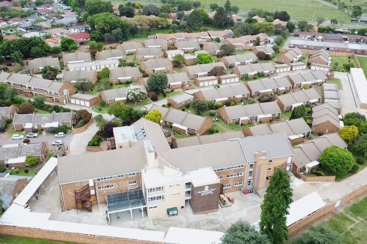 An aerial view of a residential complex featuring multiple housing units, paved driveways, and established communal gardens within a secure perimeter.