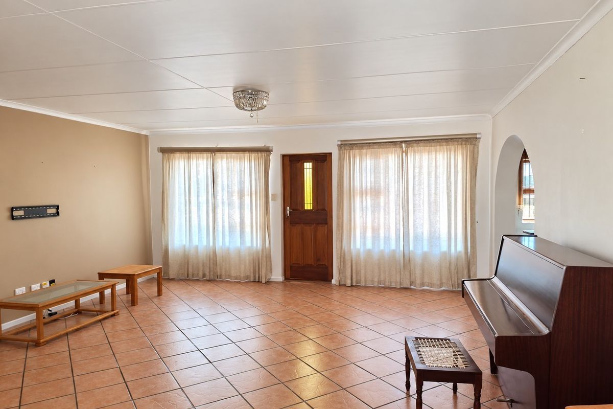 Spacious living room featuring neutral wall tones, tiled flooring, and a classic timber entrance door, offering a bright and functional layout.