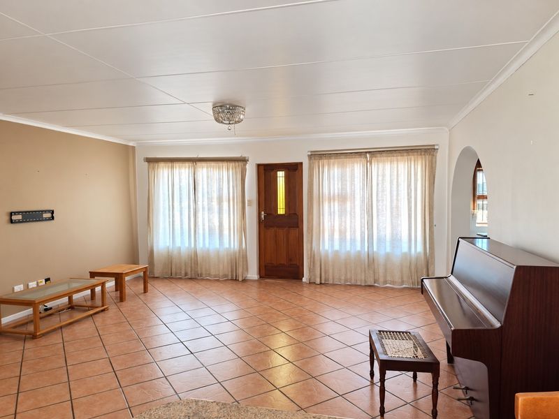 Spacious living room featuring neutral wall tones, tiled flooring, and a classic timber entrance door, offering a bright and functional layout.