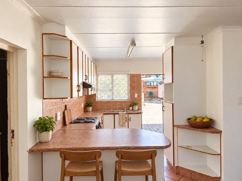 A functional kitchen featuring laminate countertops, built-in cabinetry, an electric hob, and a tiled backsplash, with direct access to an outdoor area.