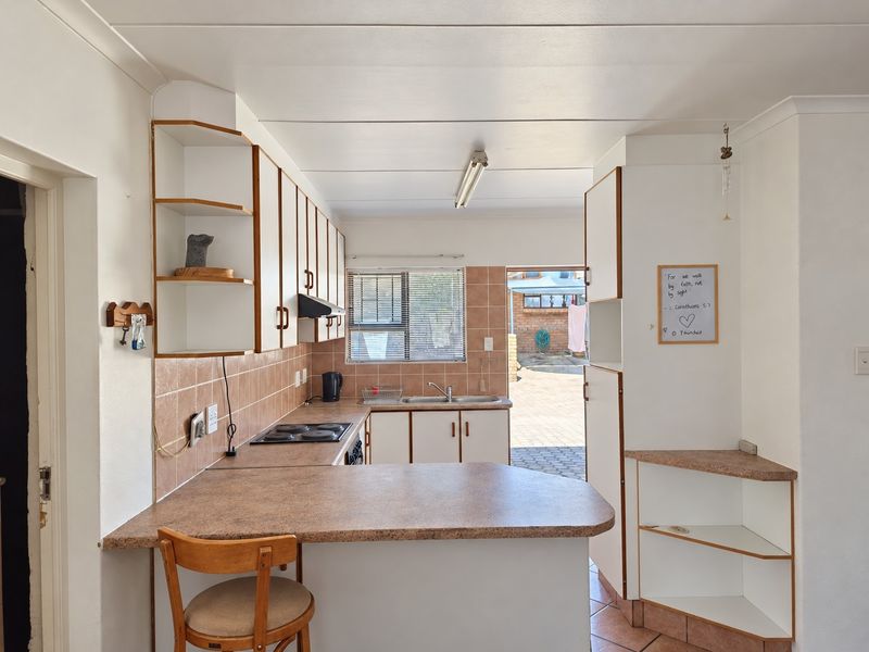 A functional kitchen featuring laminate countertops, built-in cabinetry, an electric hob, and a tiled backsplash, with direct access to the rear exterior area.