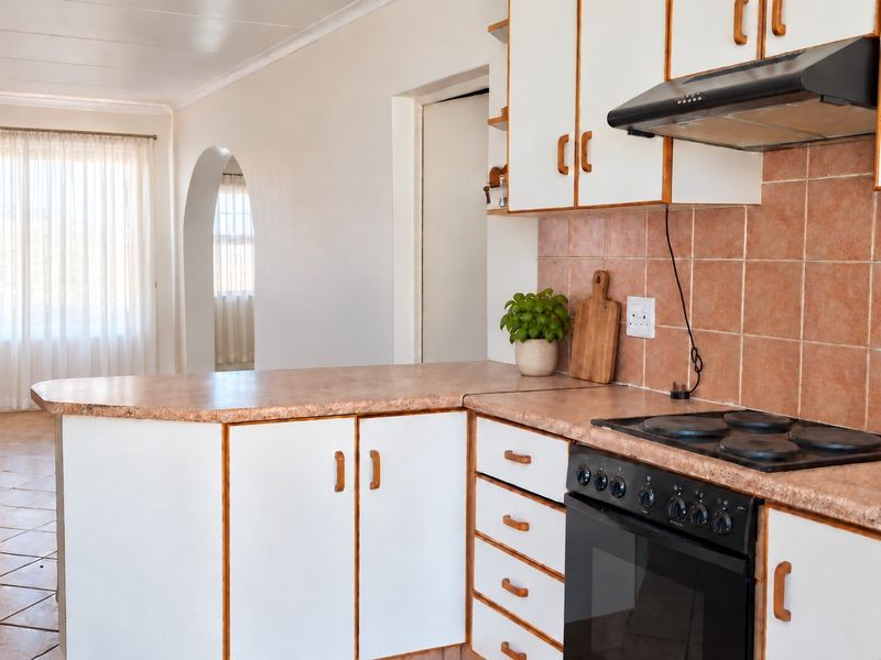 A functional kitchen featuring white cabinetry, laminate countertops, a built-in oven with hob, and a tiled backsplash, leading into an adjacent living area.