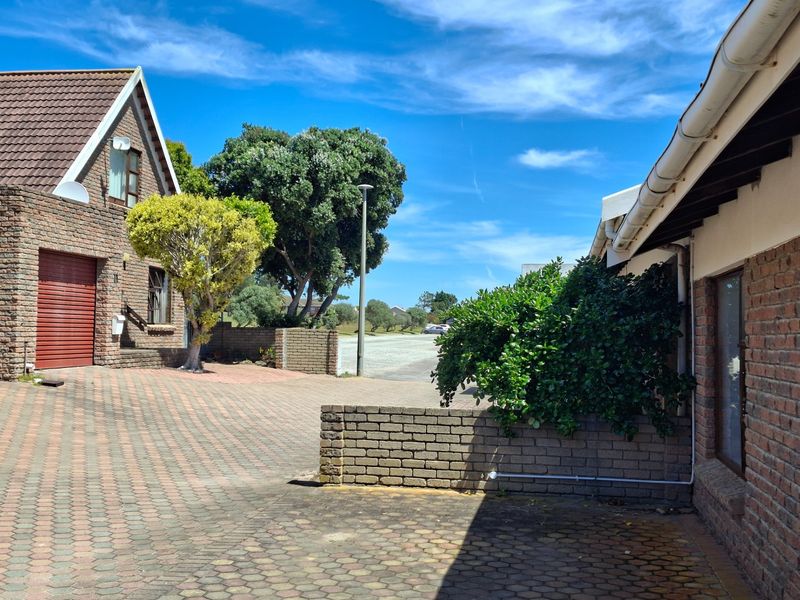 Front exterior view of a townhouse featuring a brick facade, paved driveway, and integrated garage, set within a well-maintained residential complex.