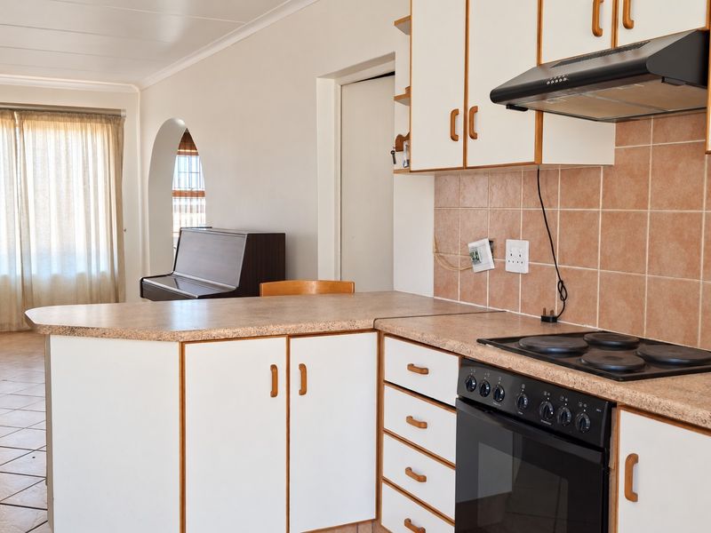 A functional kitchen featuring laminate countertops, built-in oven with hob, extractor fan, and tiled backsplash, opening into an adjacent living area via an archway.