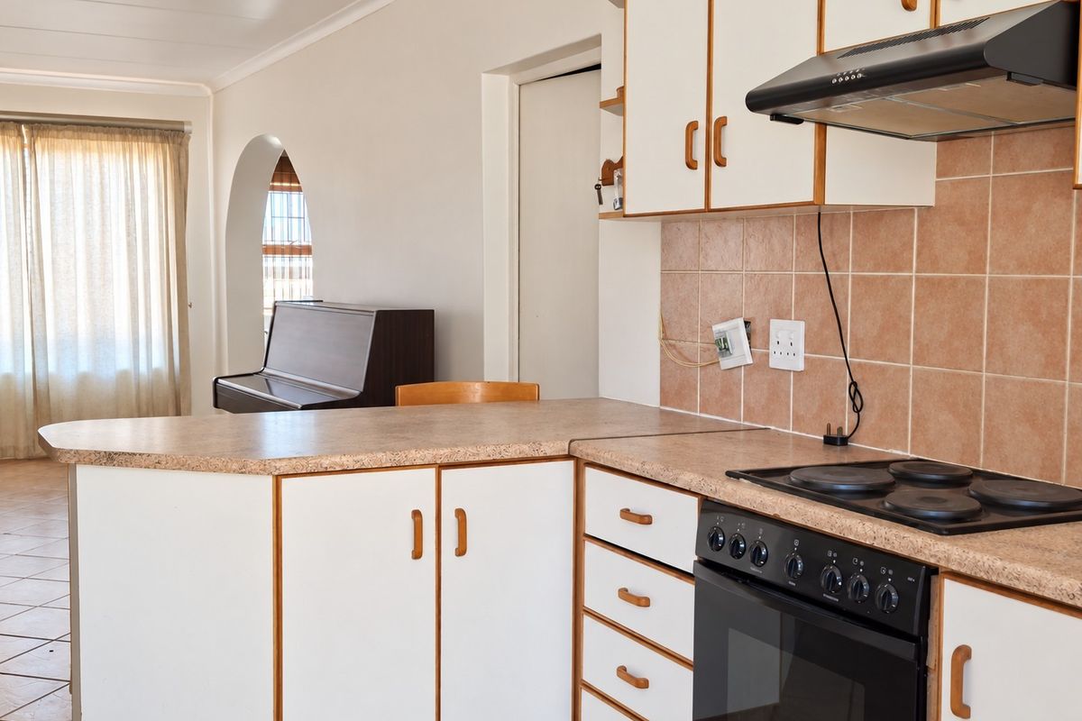 A functional kitchen featuring laminate countertops, built-in oven with hob, extractor fan, and tiled backsplash, opening into an adjacent living area via an archway.