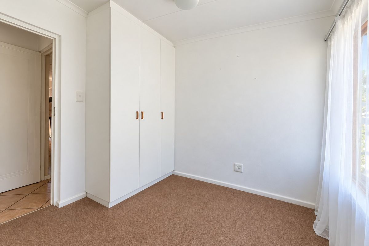 A clean, empty bedroom featuring neutral carpet flooring, a built-in wardrobe, and natural light from the window.