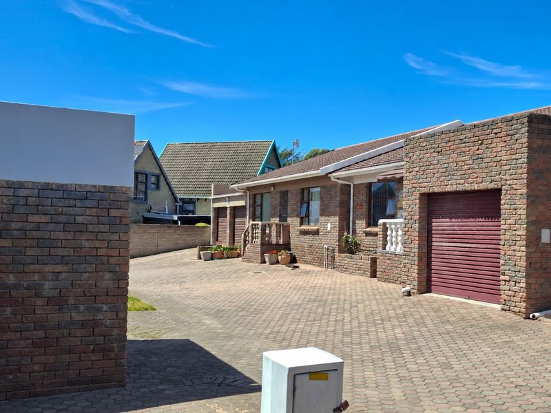 Front exterior view of a face brick townhouse complex featuring a paved driveway, roller garage doors, and tiled roofing under a clear sky.
