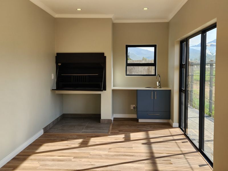 A modern, empty indoor entertainment area featuring a built-in braai, sink with base cabinetry, and large sliding glass doors leading to the exterior.