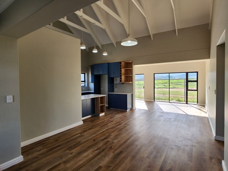 Spacious open-plan living and kitchen area featuring vaulted ceilings, modern blue cabinetry, and large sliding doors opening to a scenic rural view.