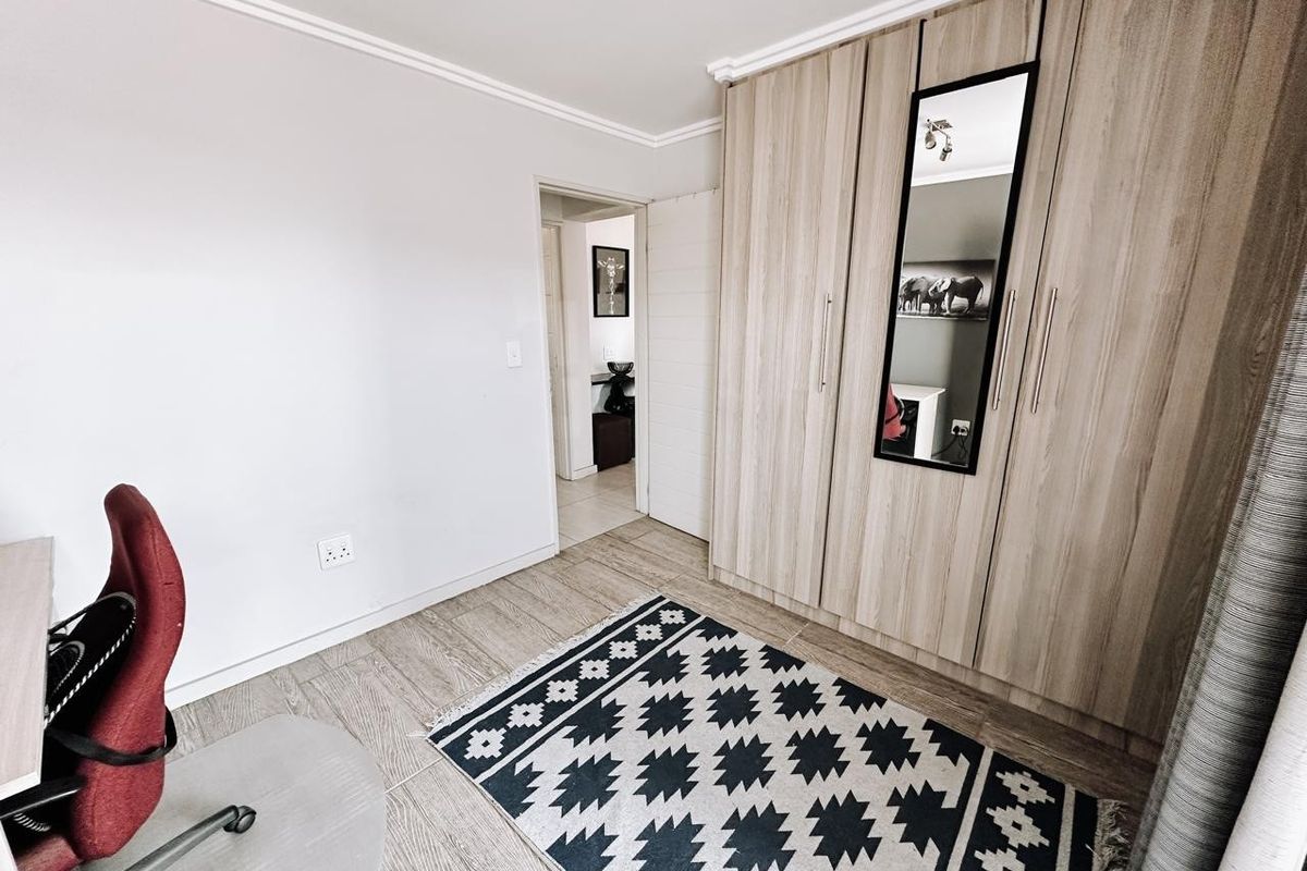 A well-maintained bedroom featuring modern wood-finish built-in cupboards, neutral wall tones, and durable tiled flooring, offering a clean and functional living space.