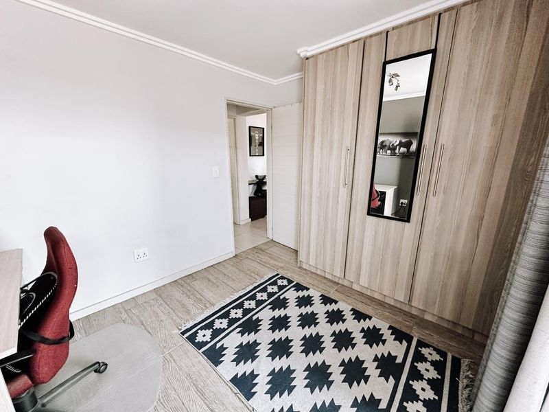 A well-maintained bedroom featuring modern wood-finish built-in cupboards, neutral wall tones, and durable tiled flooring, offering a clean and functional living space.