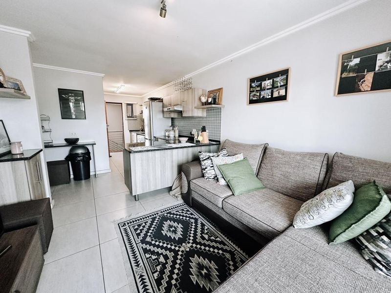 An open-plan living area featuring a modern kitchen with cabinetry and a breakfast island, seamlessly connected to the lounge space with tiled flooring.