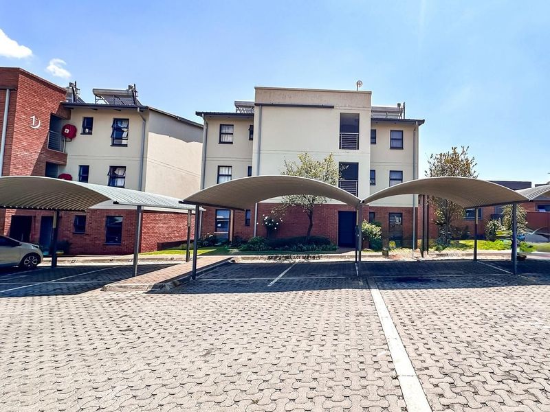 Exterior view of an apartment complex featuring paved parking bays with covered carports and brick building facades.