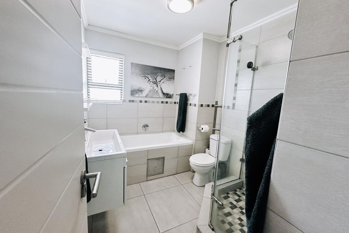 Modern bathroom featuring a built-in bathtub, separate glass-enclosed shower, wall-mounted vanity, and neutral floor-to-ceiling tiling.