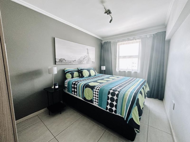 A well-maintained bedroom featuring neutral grey walls, tiled flooring, and ceiling coving, providing a clean and functional living space.