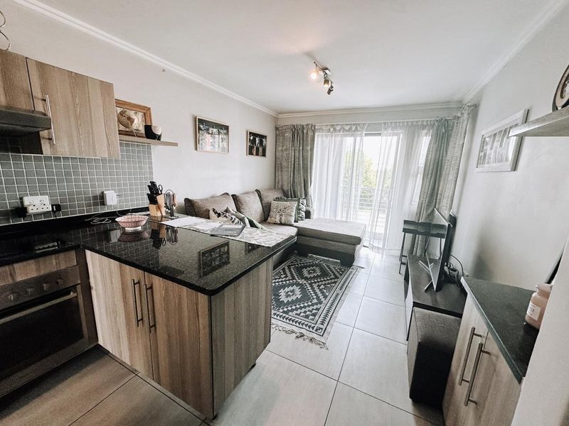 An open-plan living area featuring a modern kitchen with granite countertops and tiled flooring, seamlessly flowing into a bright lounge with balcony access.