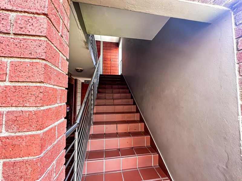 An exterior staircase featuring tiled steps, a metal handrail, and exposed brickwork leading to the apartment entrance.