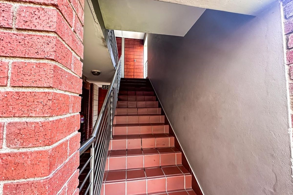 An exterior staircase featuring tiled steps, a metal handrail, and exposed brickwork leading to the apartment entrance.