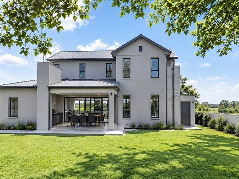 Rear view of a modern double-story home featuring a covered patio, manicured lawn, and clean architectural lines.