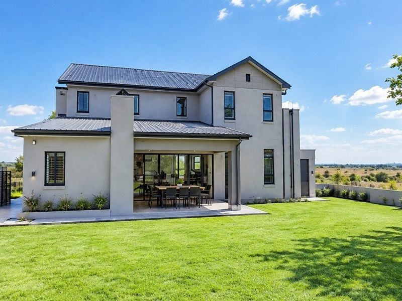 A well-maintained double-story residence featuring a covered patio, metal roofing, and a spacious landscaped garden with perimeter walling.