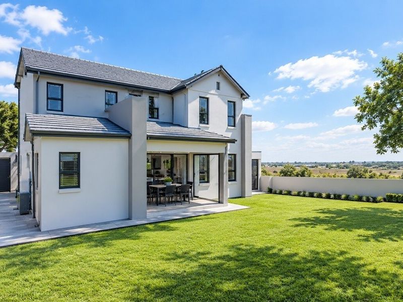 Rear view of a modern two-story house featuring a covered patio, well-maintained lawn, and perimeter boundary wall with scenic landscape views.