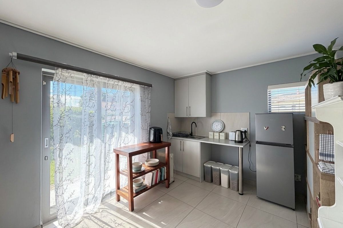A compact kitchen area featuring modern grey cabinetry, a stainless steel sink with a black mixer tap, and tiled flooring with access to a patio.