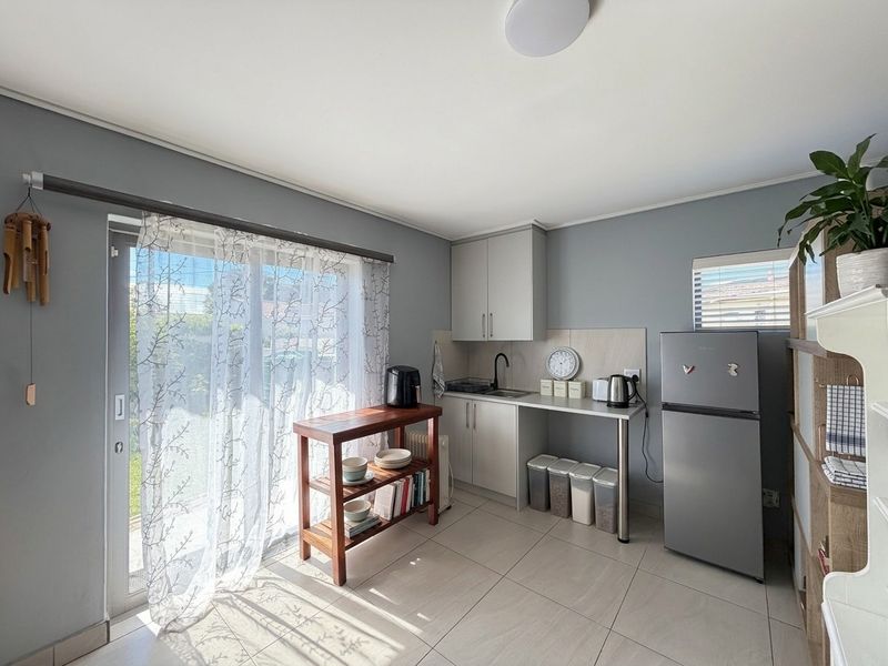 A compact kitchen area featuring modern grey cabinetry, a stainless steel sink with a black mixer tap, and tiled flooring with access to a patio.
