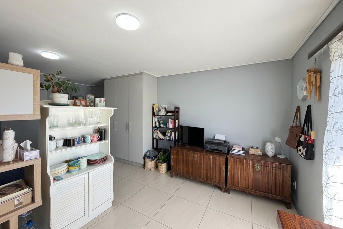 A well-maintained living area featuring neutral grey walls, light-colored floor tiles, and practical built-in storage cupboards.