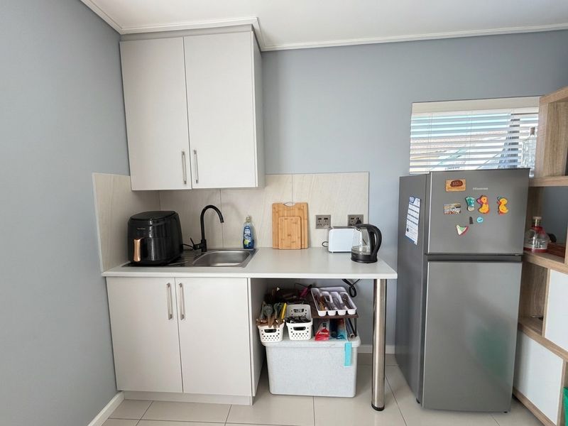 Compact kitchen area featuring modern white cabinetry, a stainless steel sink with a black mixer tap, and a tiled splashback.