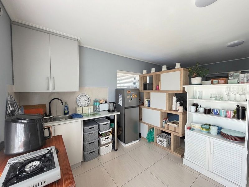 A compact kitchen area featuring built-in cabinetry, a stainless steel sink with a modern mixer tap, and neutral tiled flooring.
