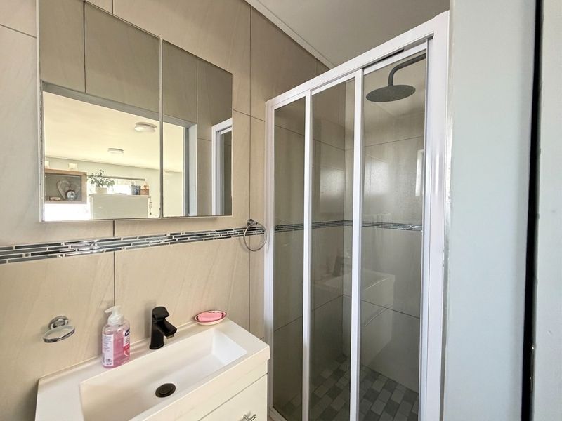 Modern bathroom featuring a glass-enclosed shower with a rain shower head, a vanity basin, and a wall-mounted mirror cabinet with tiled finishes.