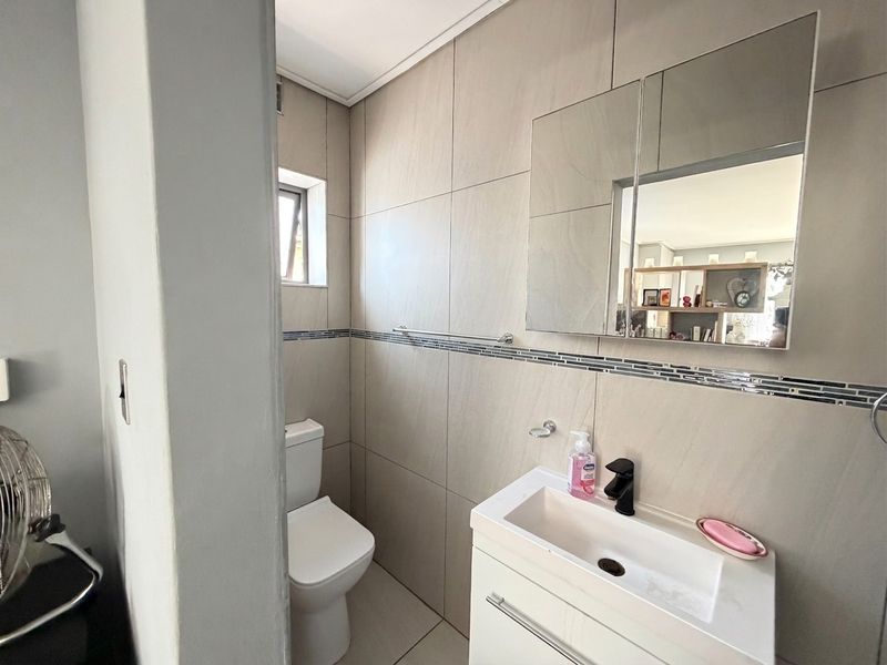 A modern bathroom featuring a vanity cabinet with basin, wall-mounted mirror cabinet, toilet, and neutral floor-to-ceiling wall tiles.
