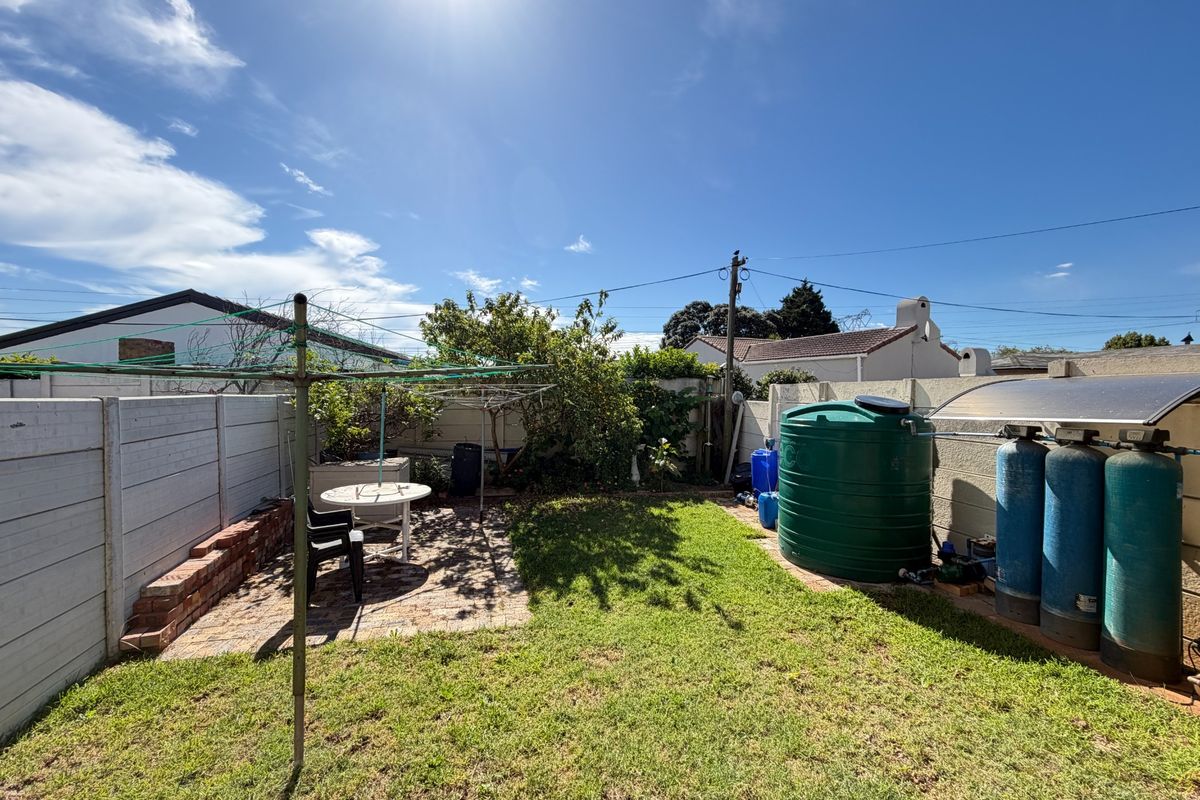 A rear garden area featuring a paved patio, lawn, precast boundary wall, and installed water storage and filtration infrastructure.